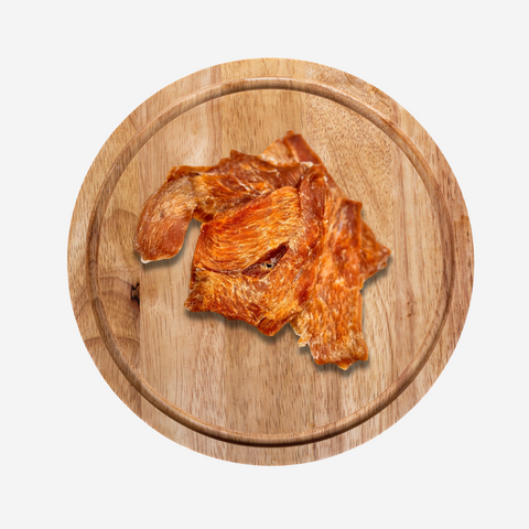 A round wooden chopping board displaying a pile of Chicken Jerky Treats for dogs